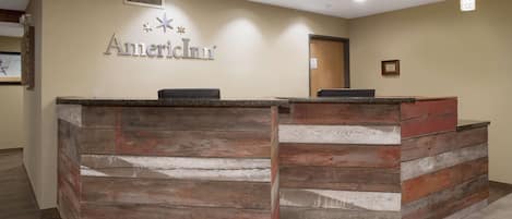 A reception desk with a wooden design, a sign reading "AmericInn", and a tiled floor.