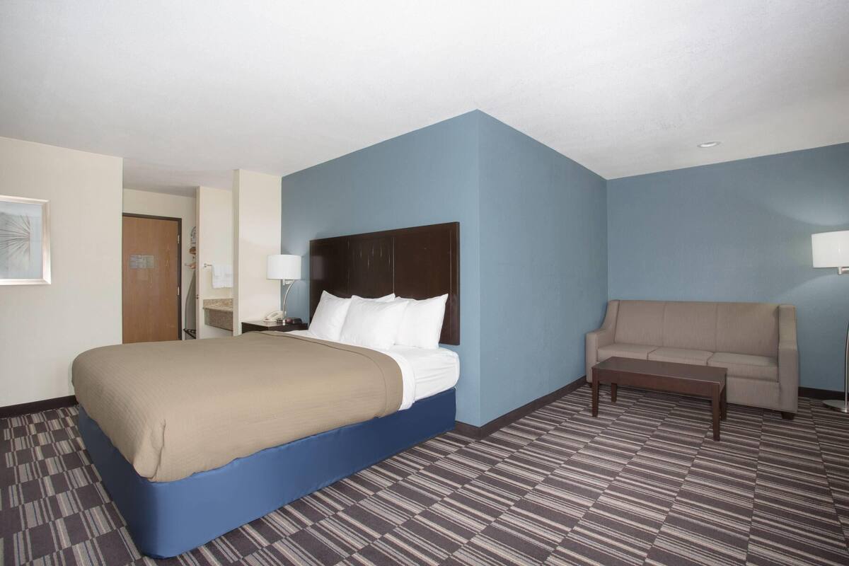 A hotel room with a large bed, a sofa, a nightstand, and a lamp.