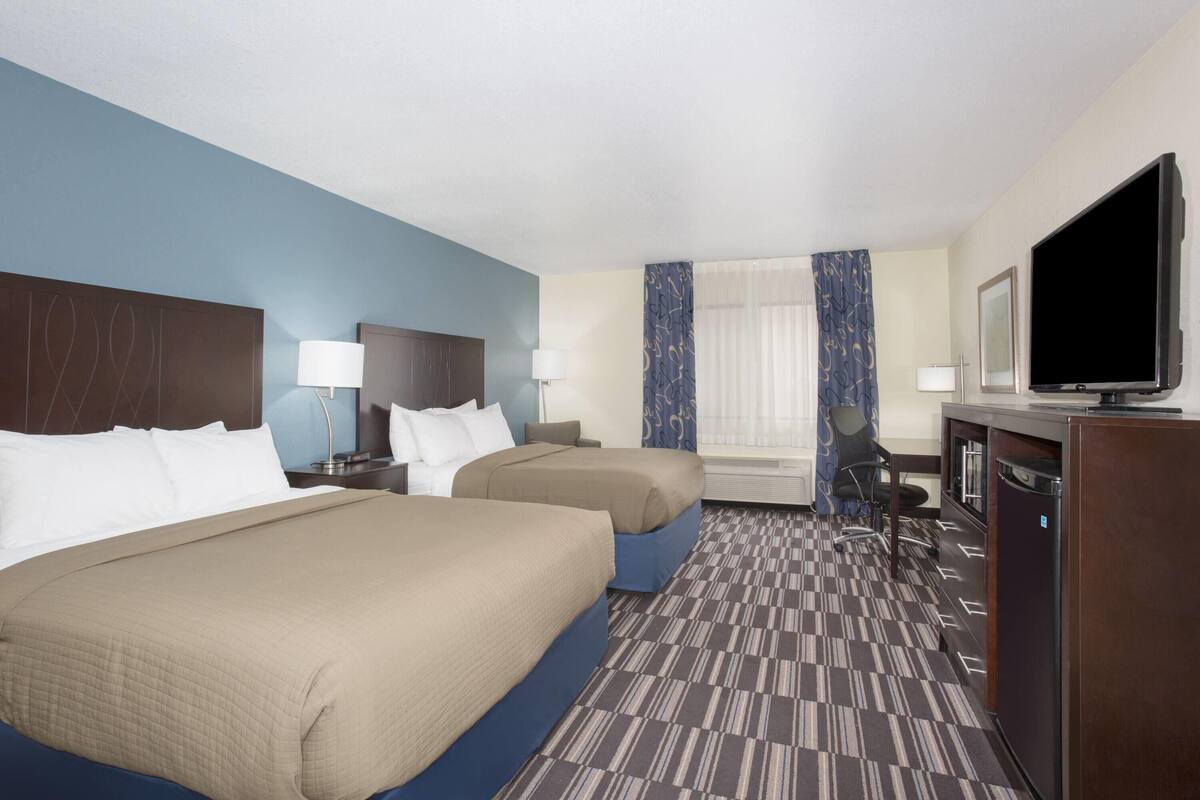 A hotel room with two beds, a desk, a television, and a window with curtains.