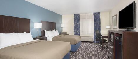A hotel room with two beds, a desk, a television, and a window with curtains.