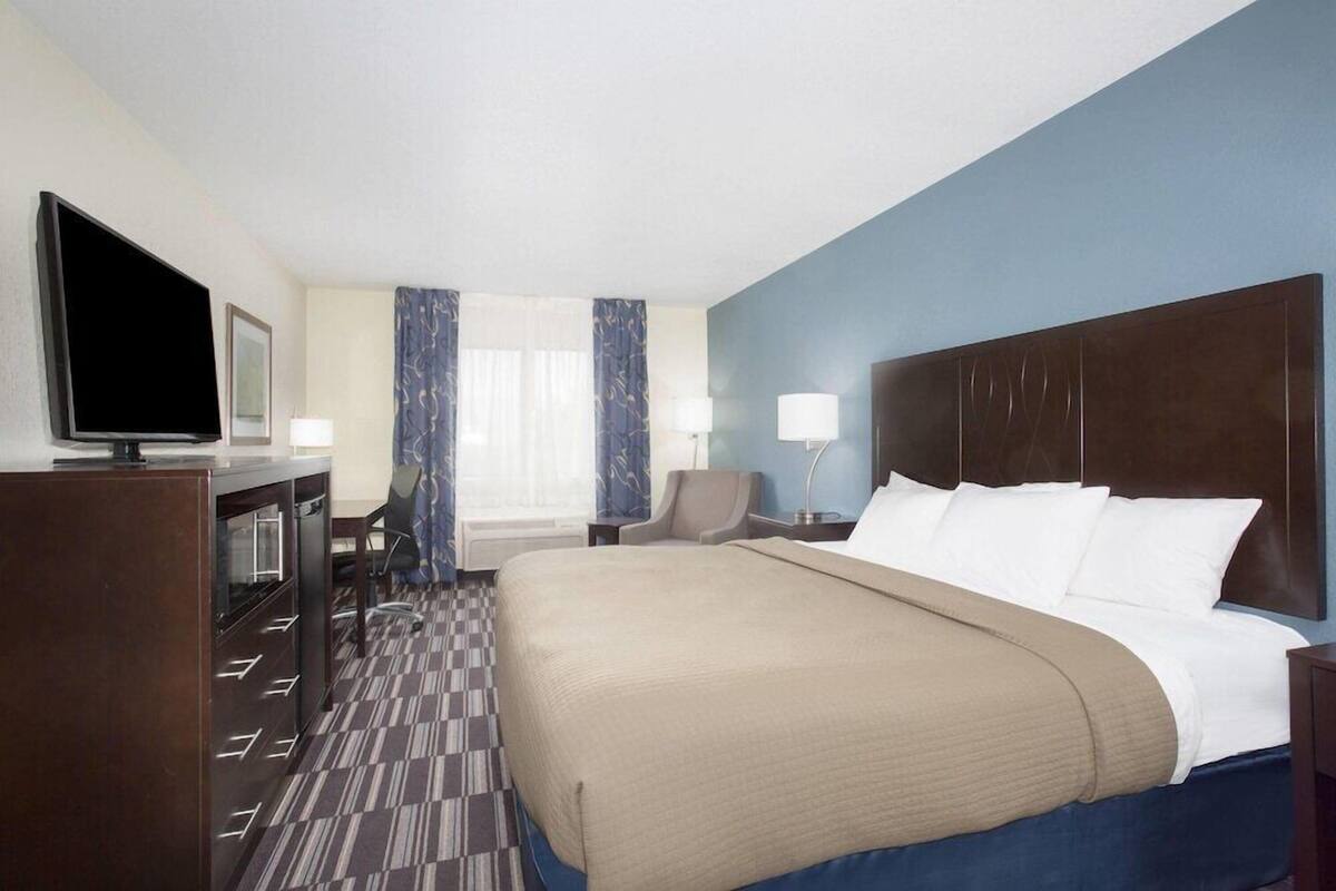 A hotel room with a large bed, a television, a desk with drawers, a chair, and a window with curtains.
