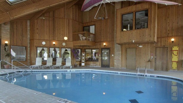 An indoor swimming pool with a wooden interior, a sunbed area, and a covered seating area. - Baymont by Wyndham Whitewater (Whitewater)