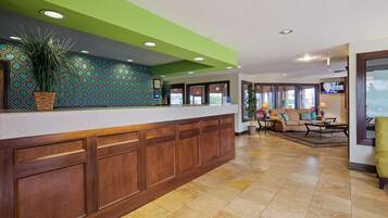 A reception area with a wooden reception desk, a green accent wall, and a seating area with a sofa and a table.