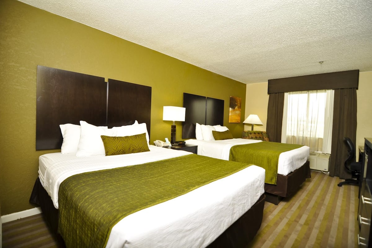 A hotel room with two beds, a desk, a chair, and a window with curtains.