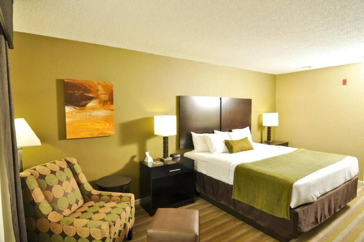 A hotel room with a bed, two bedside tables, a chair, a painting, and a lamp.