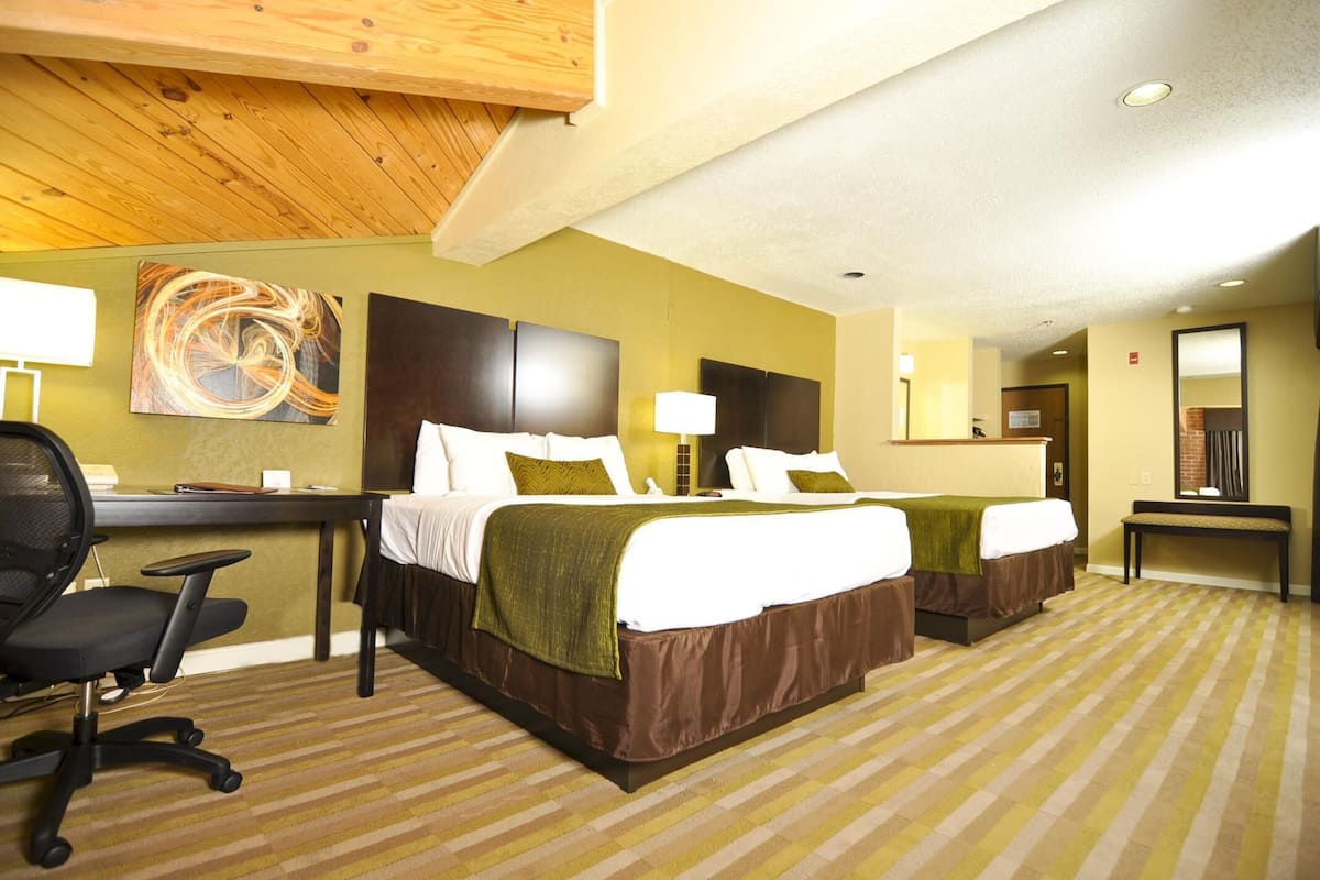 A hotel room with two beds, a desk, a chair, and a large abstract painting on the wall.