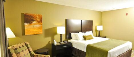 A hotel room with a bed, two bedside tables, a chair, a small table, and a painting on the wall.