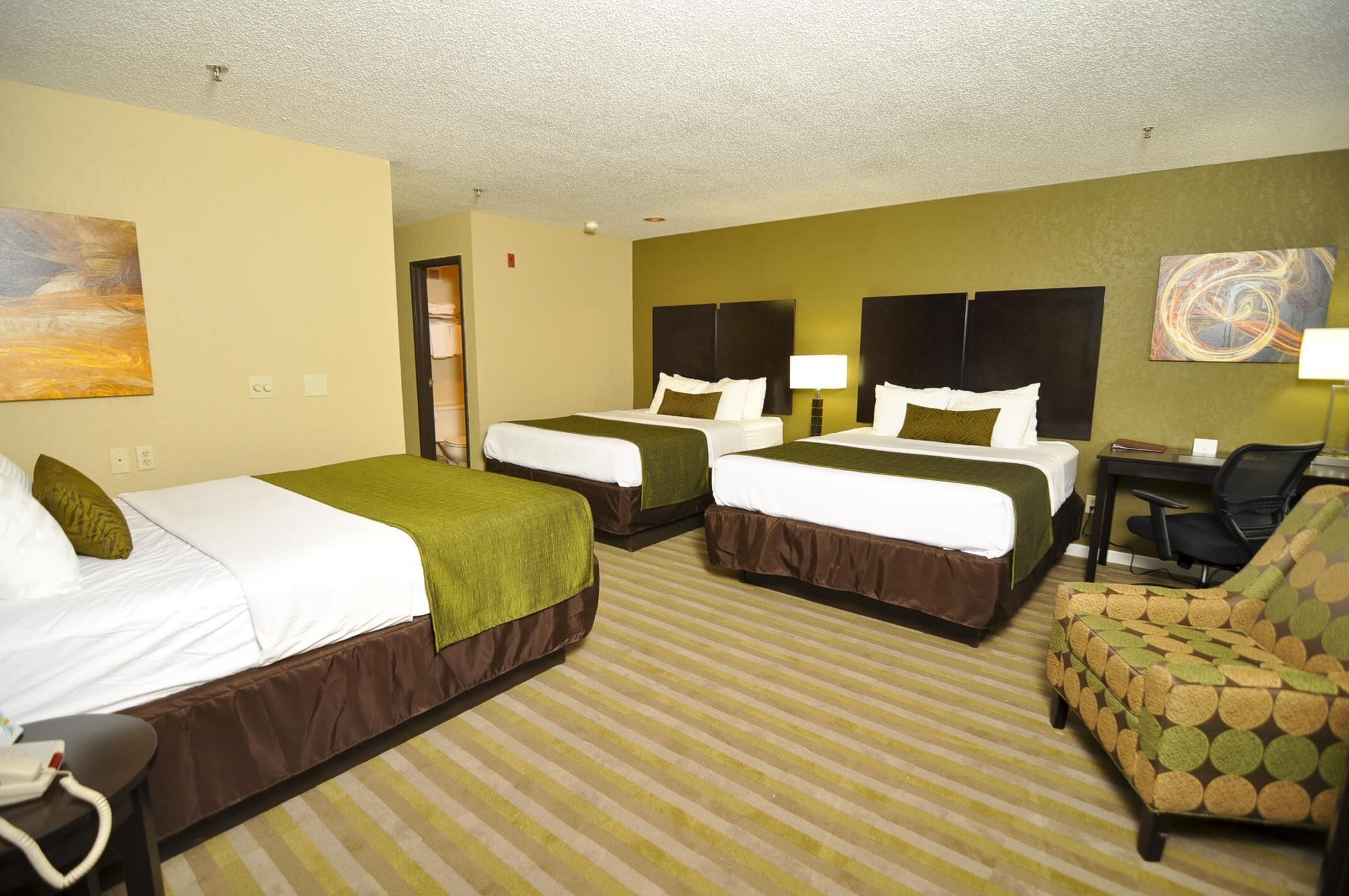 A hotel room with two beds, a desk, a chair, and artwork on the walls.