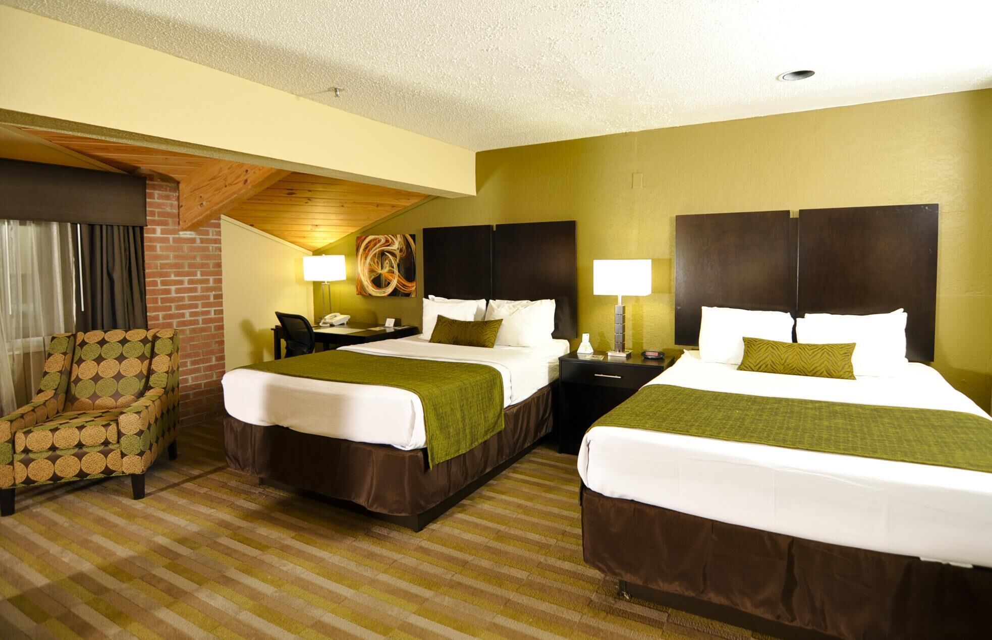 A hotel room with two beds, a chair, a desk, and a lamp.