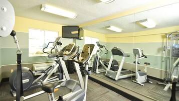 Un gimnasio con cintas de correr, elípticas y un espejo grande.