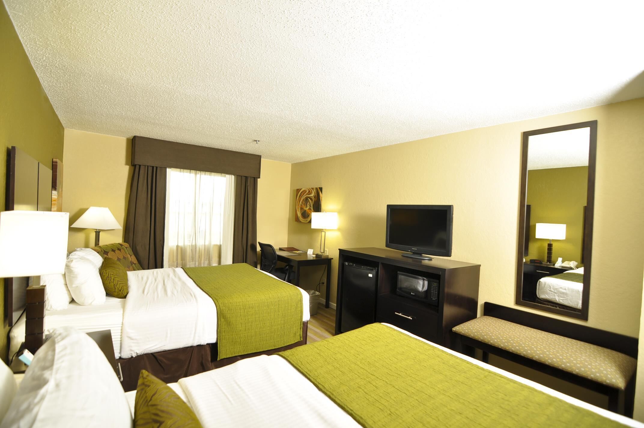 A hotel room with two beds, a desk, a television, and a mirror.