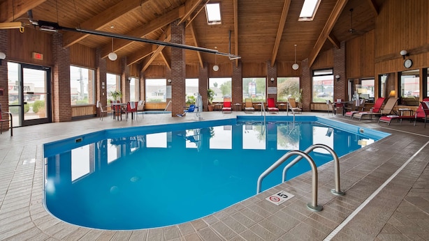 Una piscina interior con techo de madera, paredes de vidrio transparente y suelo de baldosas.