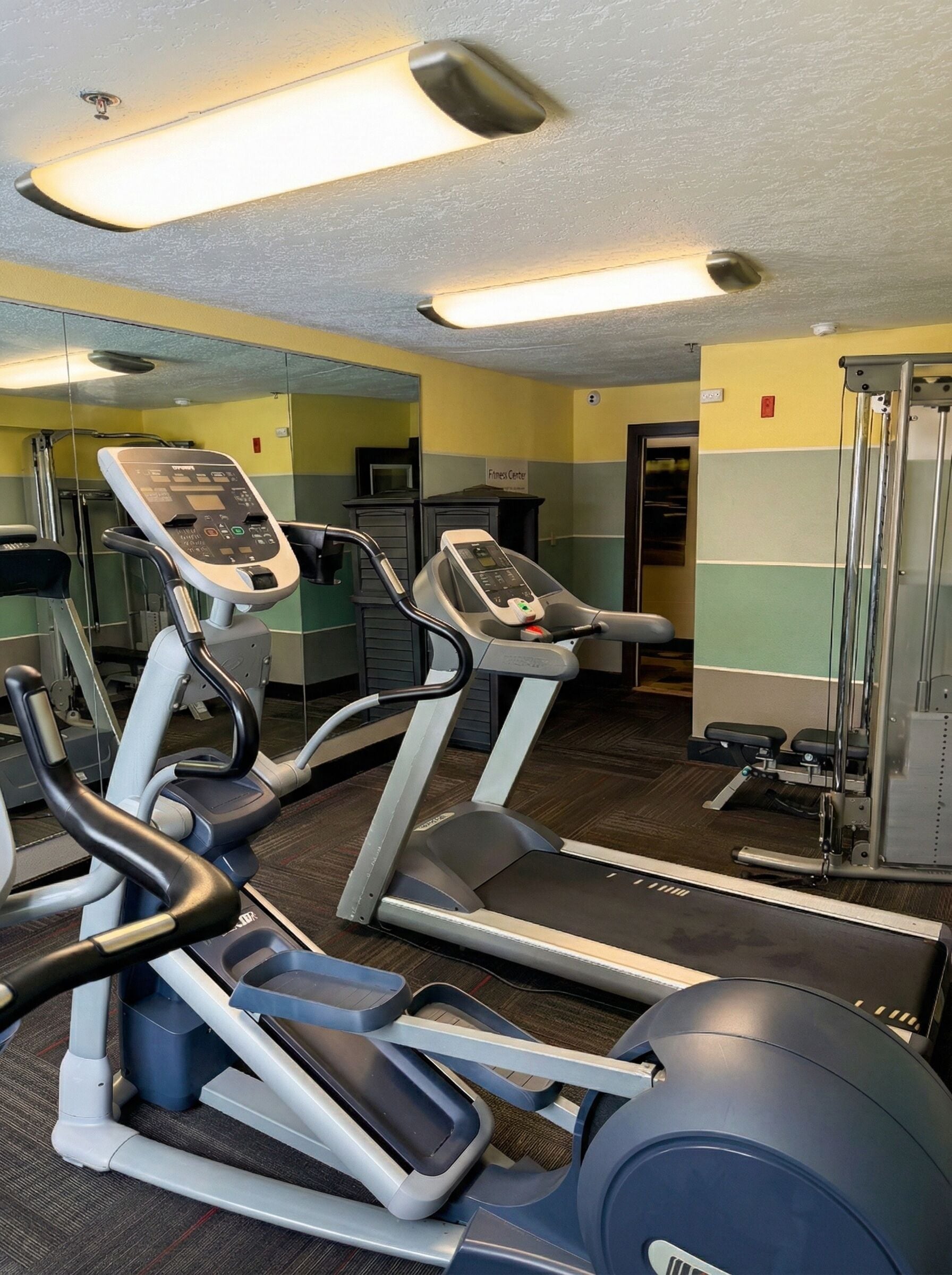 Un gimnasio con cintas de correr, un espejo grande y el letrero de centro de acondicionamiento físico.