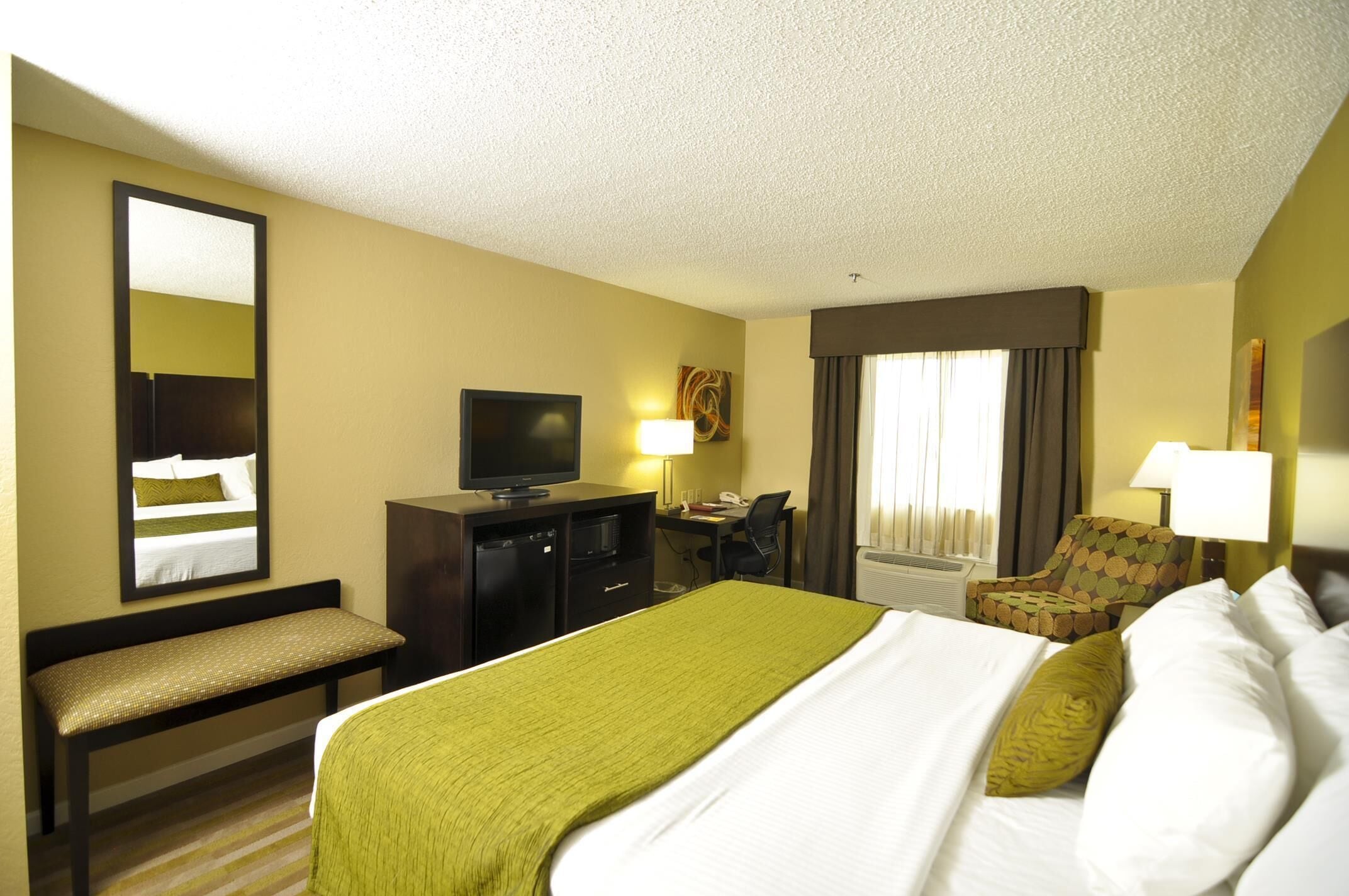 Une chambre d’hôtel comprenant un lit, un bureau, une télévision, une chaise et un banc.