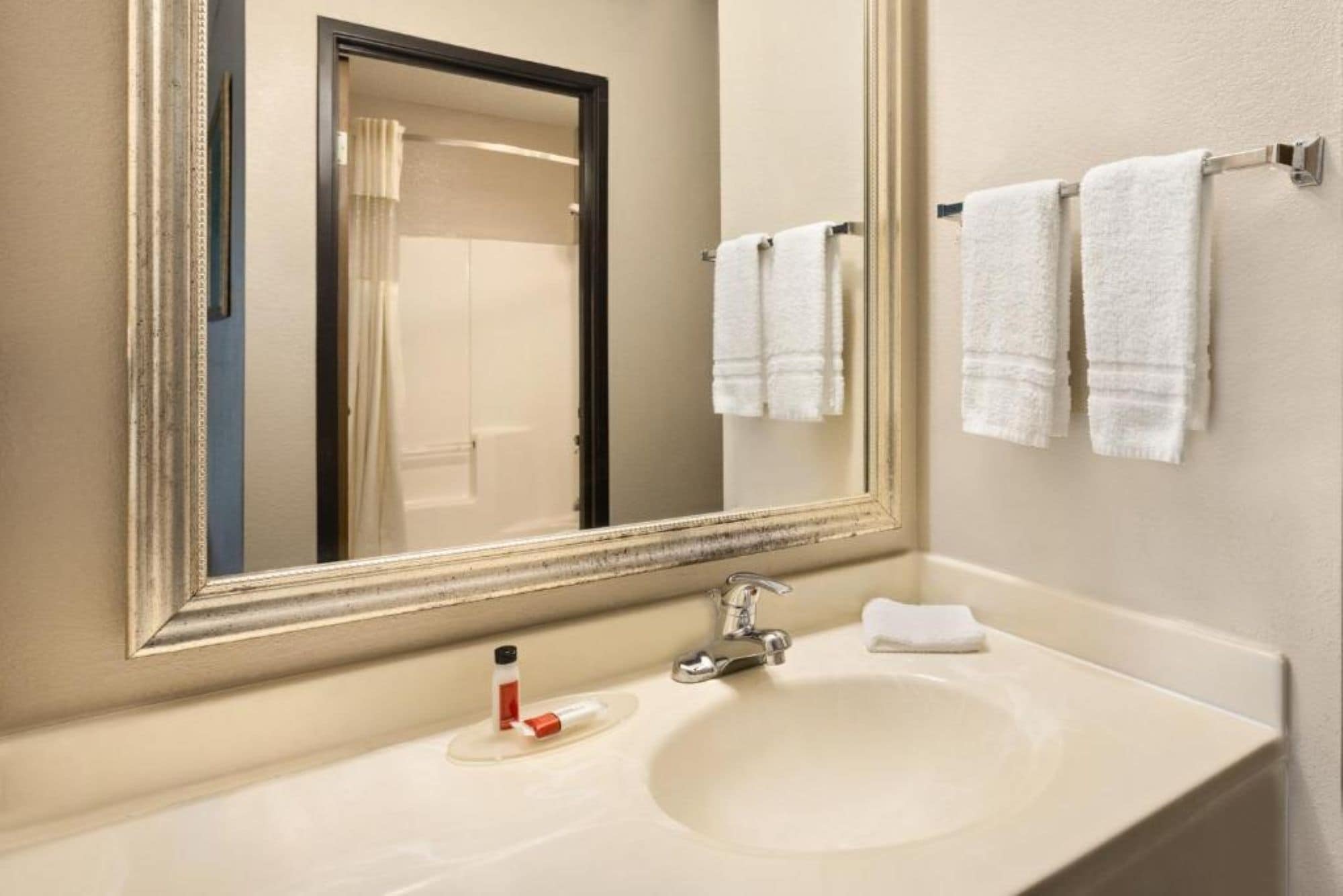 A bathroom with a large mirror, a sink, and two towels hanging on a rack.