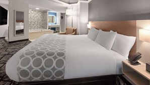A hotel room with a large bed, a bedside table with a phone, a chair, a bathroom with a mirror and sink, and a patterned carpet.