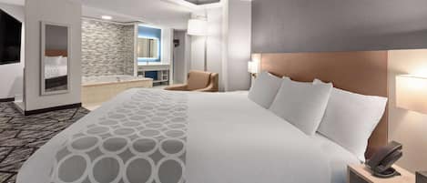 A hotel room with a large bed, a bedside table with a phone, a chair, a bathroom with a mirror and sink, and a patterned carpet.