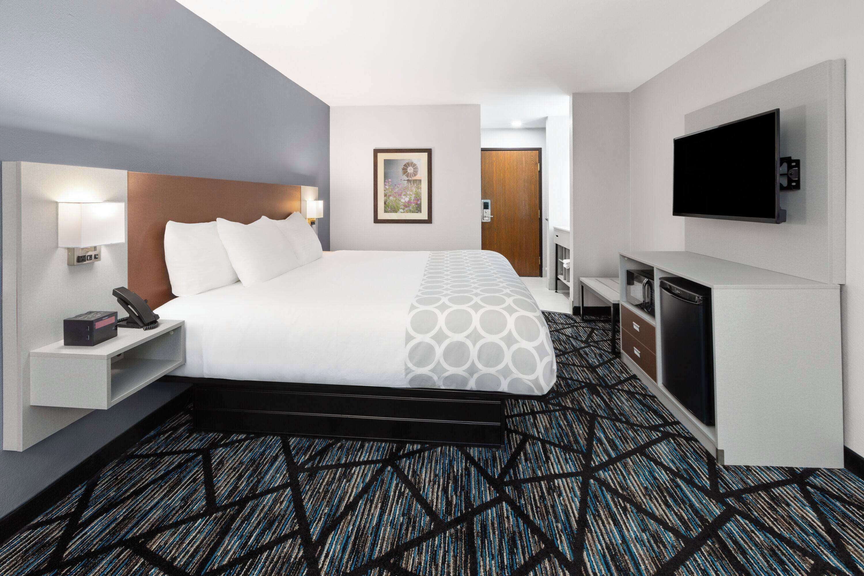 Habitación de hotel con una cama grande, un televisor de pantalla plana en la pared, un escritorio con teléfono y una alfombra estampada.