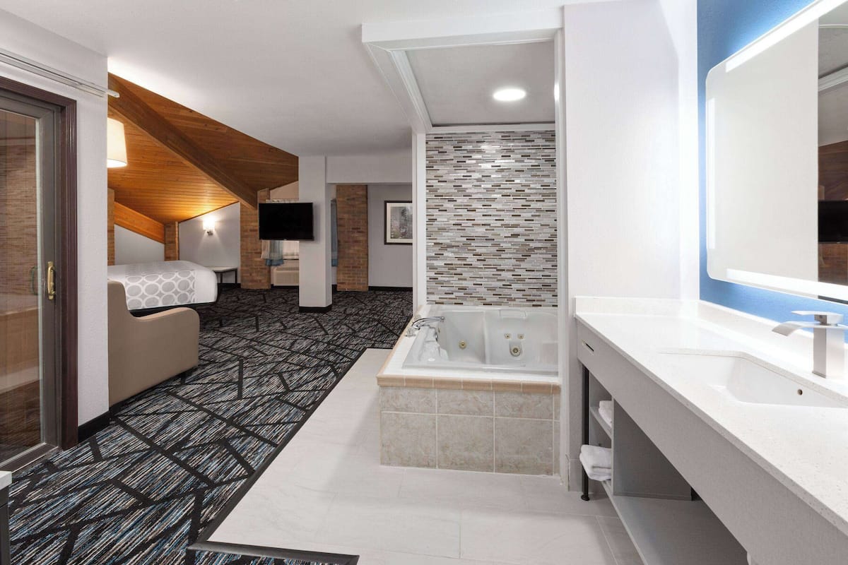 A modern hotel room with a large bed, a separate sitting area, a bathtub, and a large mirror.