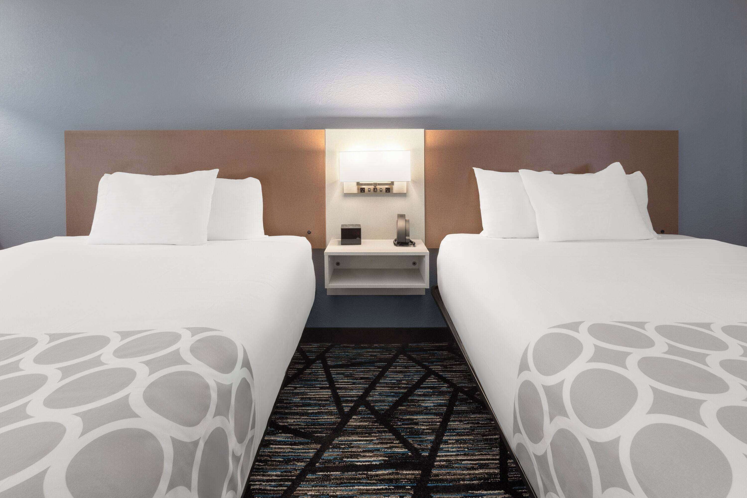 Ein Hotelzimmer mit zwei Betten, einem Nachttisch, einer Lampe und einem gemusterten Teppich.