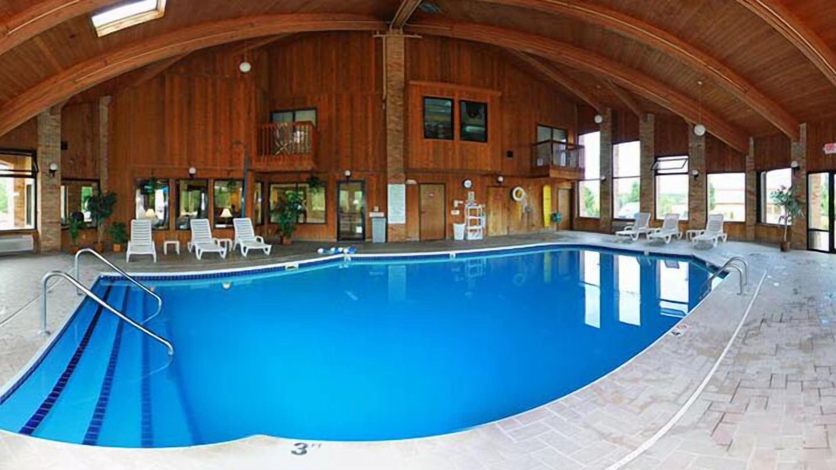 An indoor swimming pool with a wooden interior, lounge chairs, and a brick floor.