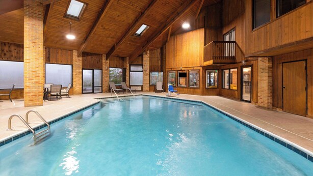 An indoor swimming pool with a wooden interior, clear blue water, and a few lounge chairs.