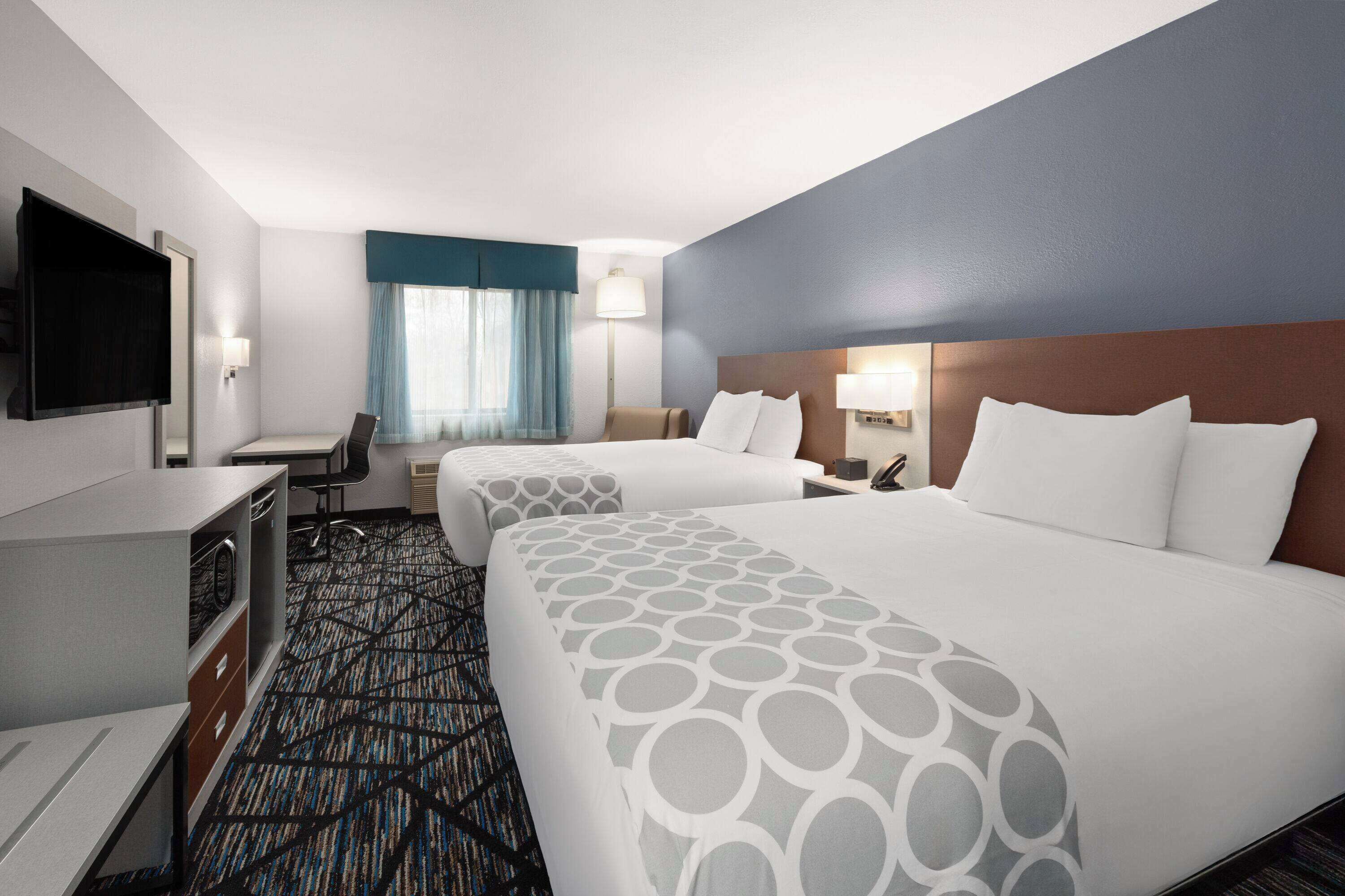 A hotel room with two beds, a desk, a chair, a TV, and a window with curtains.