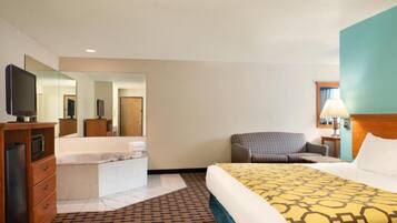Quarto de hotel com cama, escrivaninha com televisão, cadeira, banheiro com espelho e luminária.