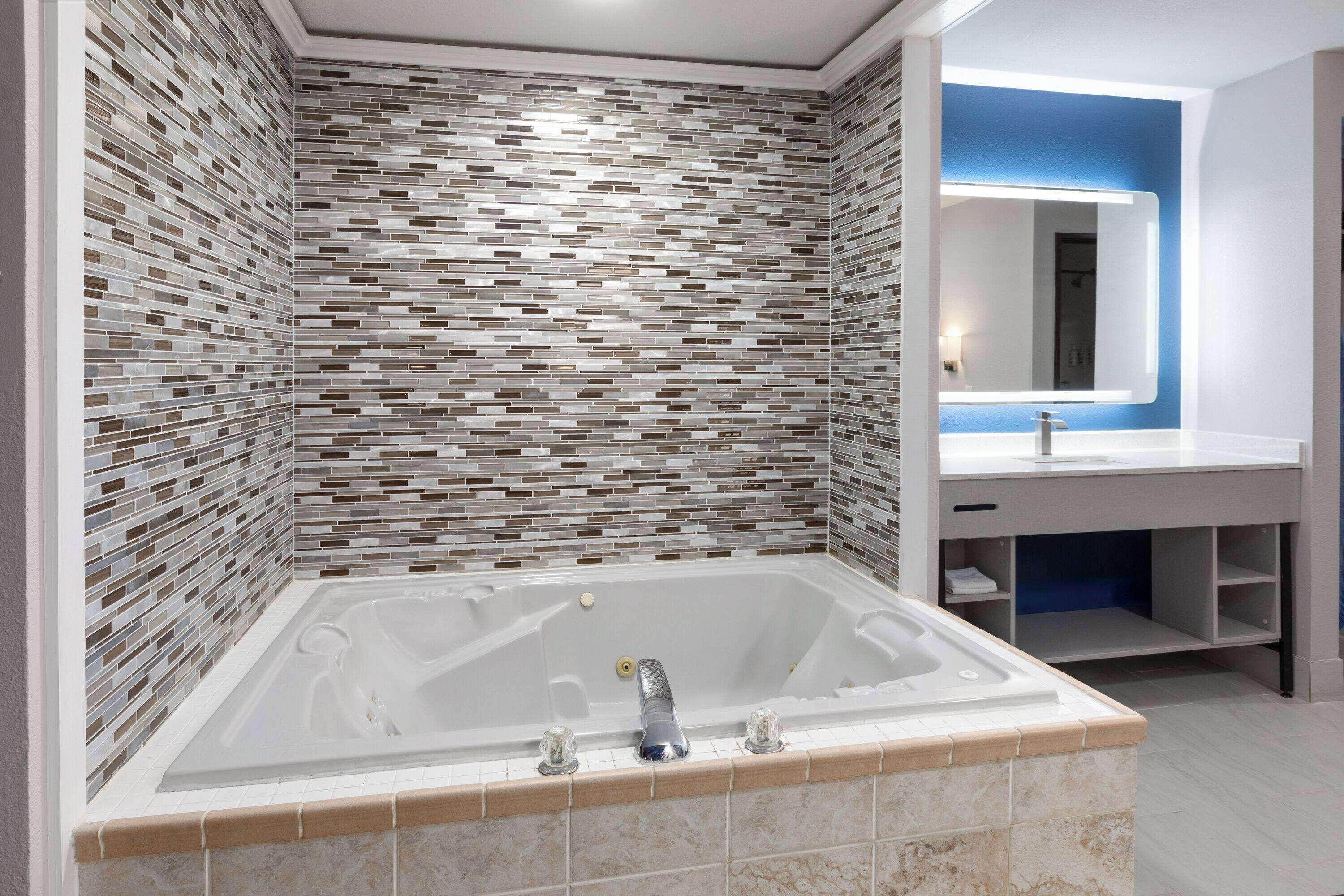 A modern bathroom with a mosaic tile wall, a freestanding bathtub, and a vanity with a mirror.