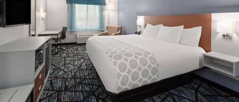 Habitación de hotel con una cama grande, un escritorio, una silla, un televisor y una ventana con cortinas.