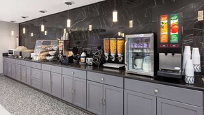 A modern kitchen area with a marble backsplash, a coffee machine, a refrigerator, and a juice dispenser.