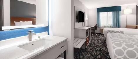 A hotel room with a large bed, a desk, a TV, a bathroom with a sink and mirror, and a patterned carpet.