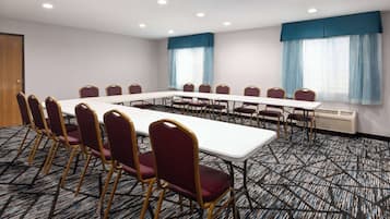 A conference room with a long table and chairs, carpeted floor, and large windows with curtains.