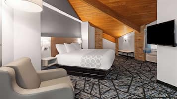 A hotel room with a bed, a chair, a TV, and a patterned carpet.