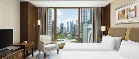 A hotel room with a large bed, a TV, a desk, and a chair. The room has a city view through large windows.