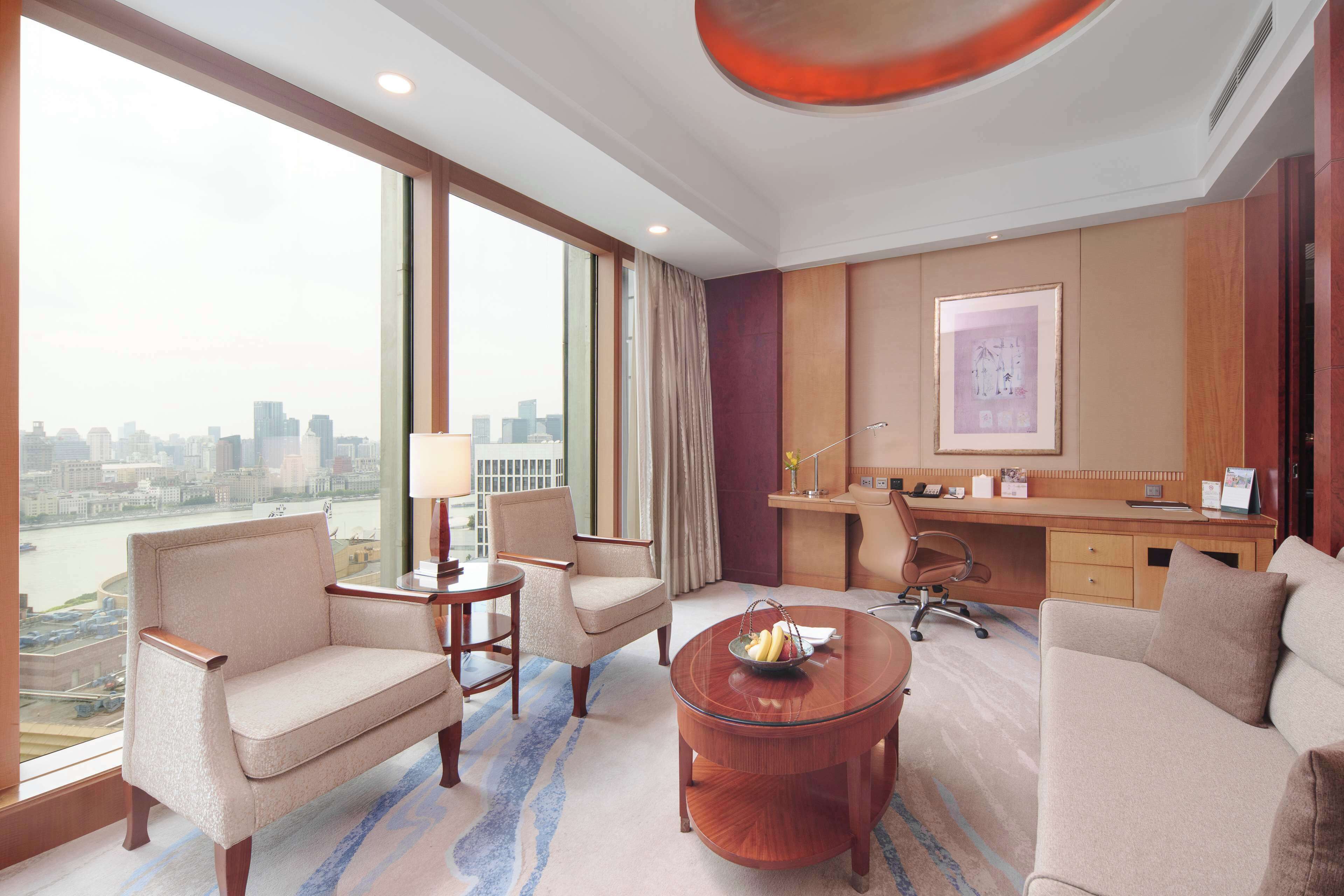 A hotel room with a large window, a desk, a sofa, and a coffee table.
