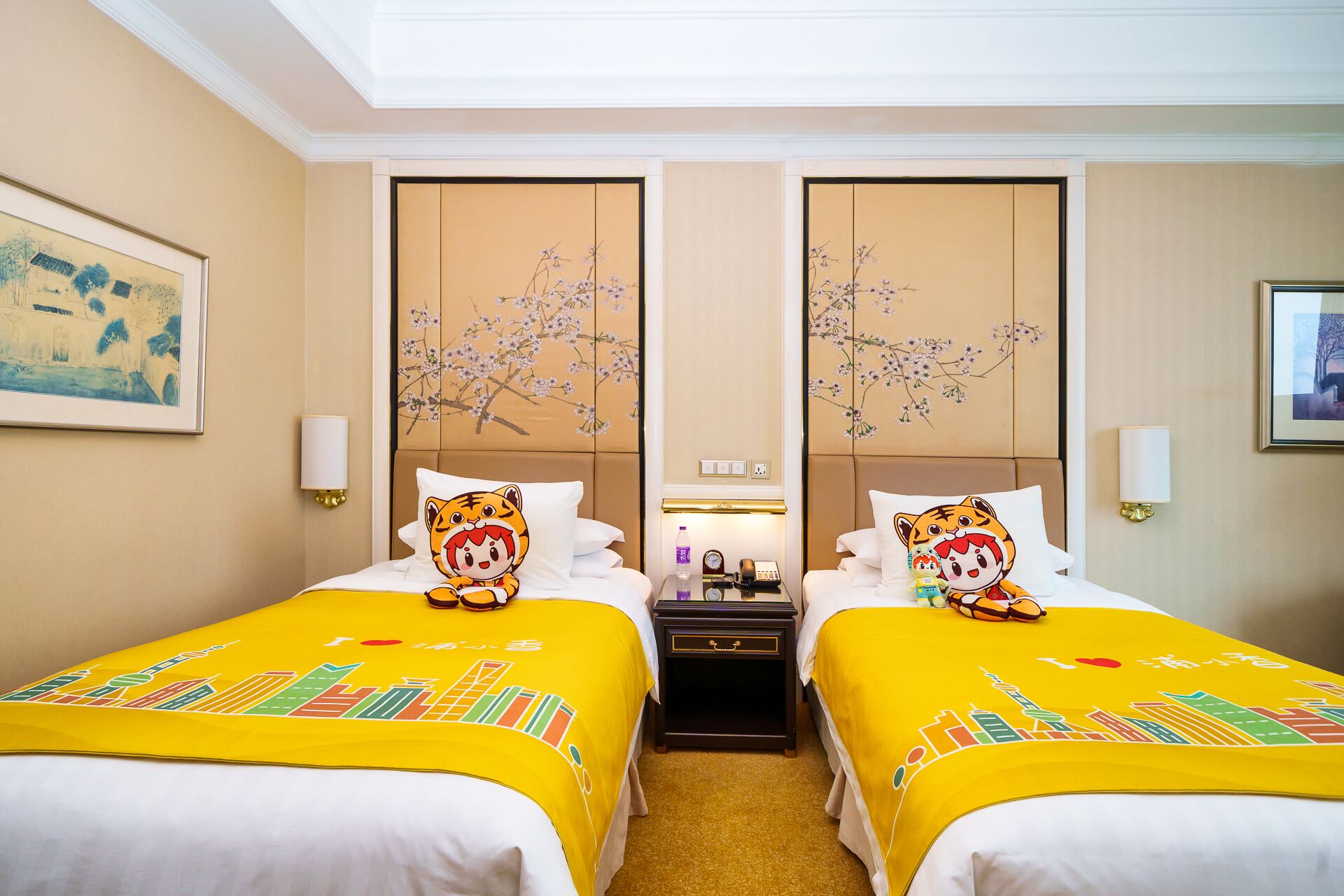 A hotel room with two beds, each with a tiger-themed pillow, a nightstand with a clock and a bottle, and a painting on the wall.