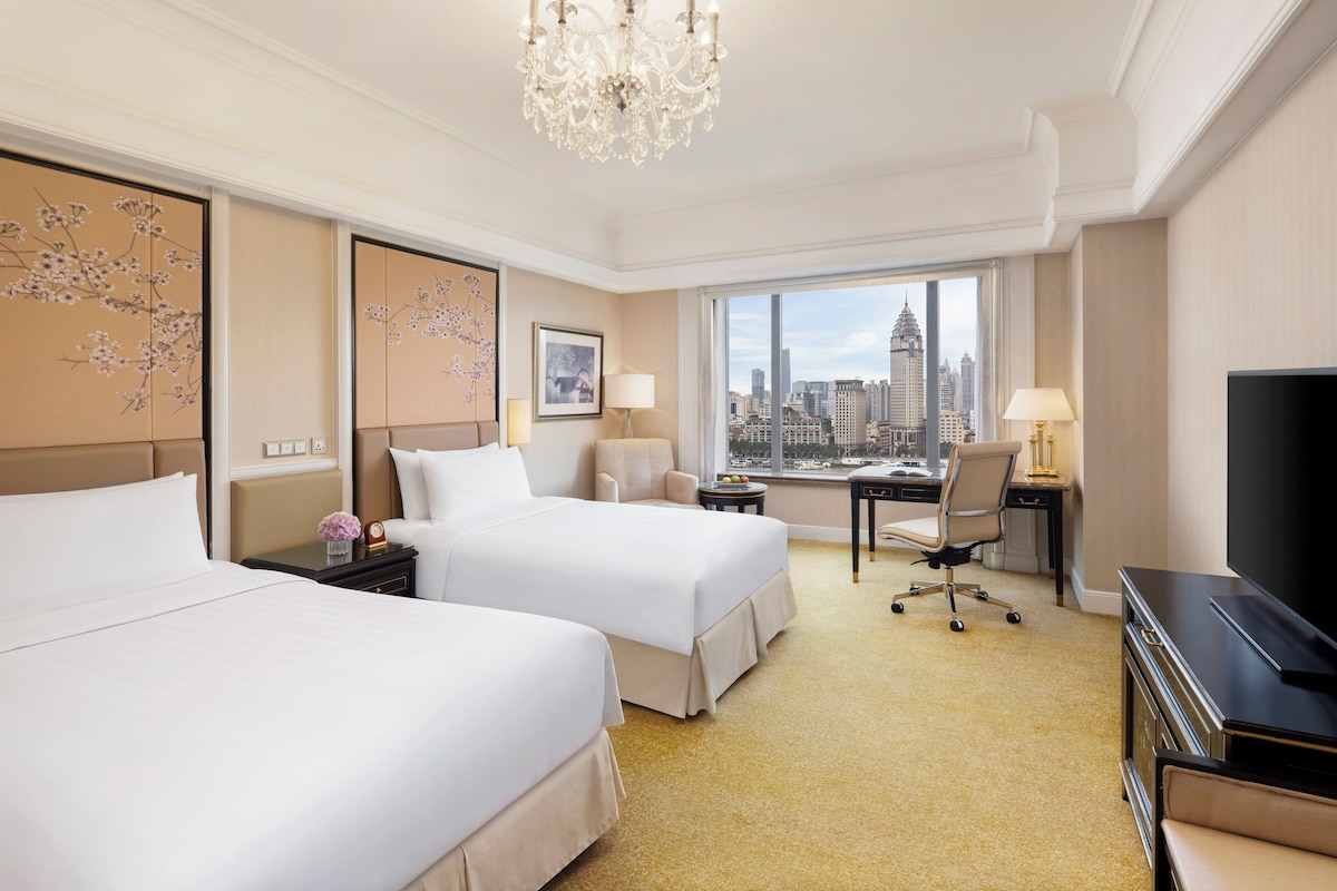 Une chambre d’hôtel avec deux lits, un bureau, une chaise, une télévision et une vue sur le paysage urbain.