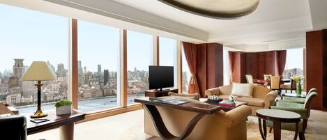 Une chambre d’hôtel spacieuse offrant une vue imprenable sur la ville, avec un canapé confortable, un bureau doté d’une lampe et un téléviseur.