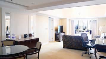 A hotel room with a dining table, chairs, a sofa, a TV, and a city view.