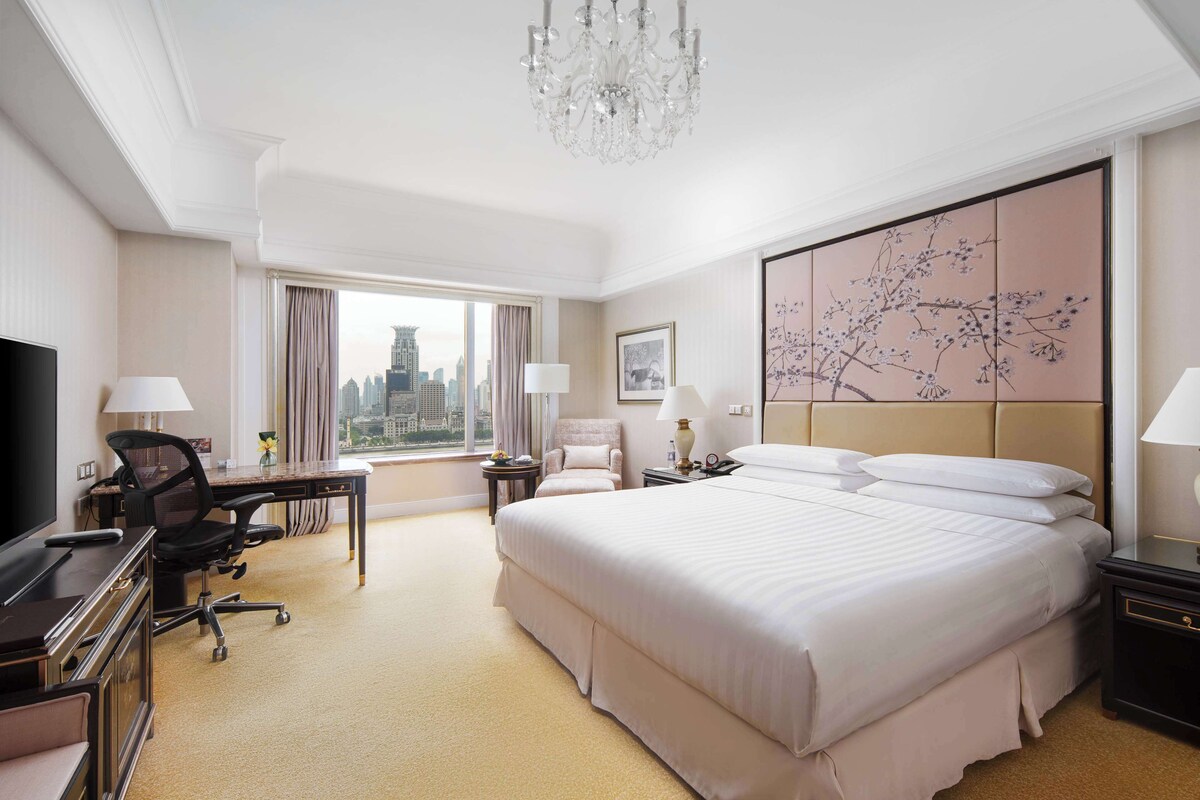 Une chambre d’hôtel avec un grand lit, un bureau, une chaise, une télévision et une vue sur la ville.