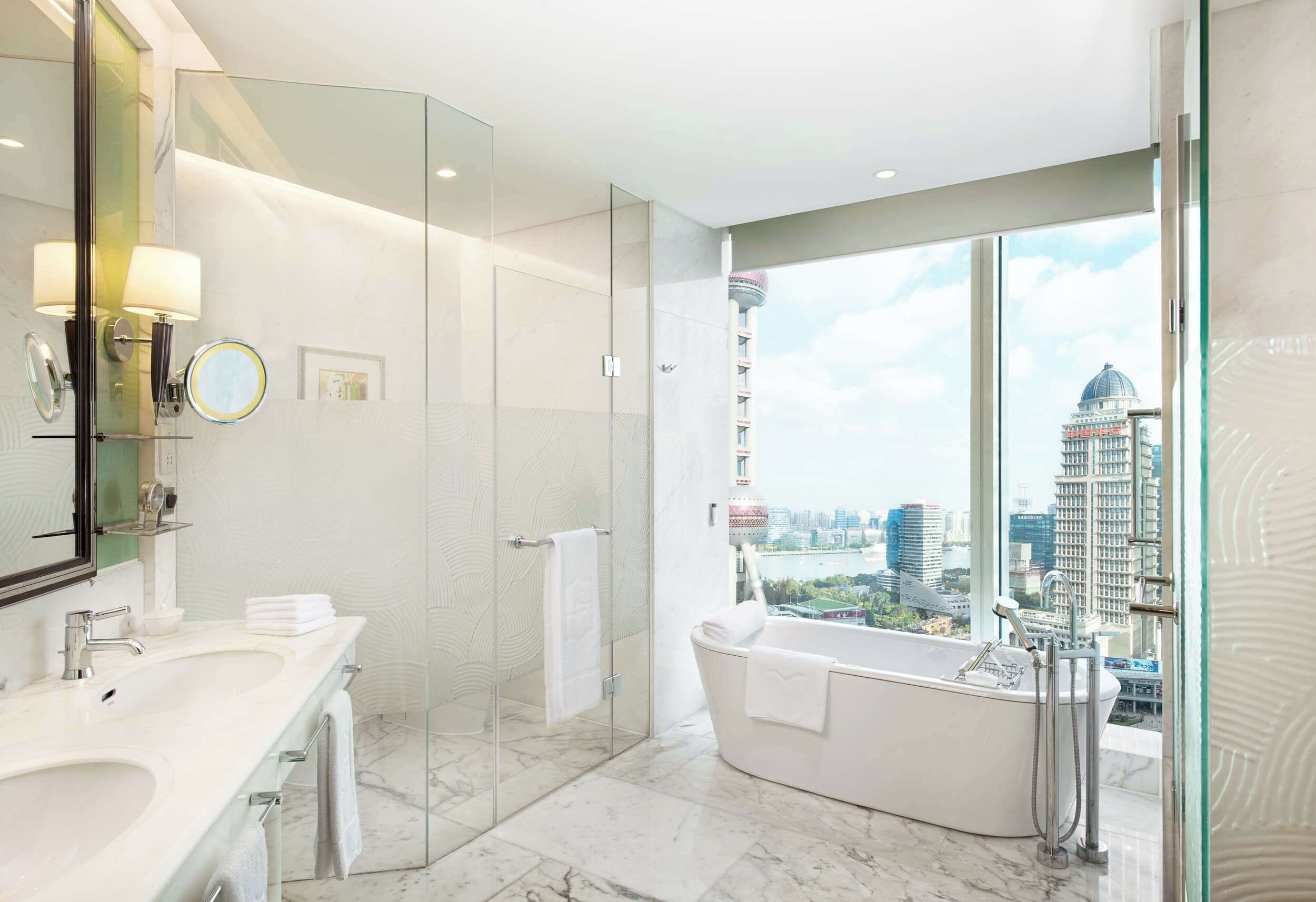 A modern bathroom with a large bathtub, a glass-enclosed shower, and a city view.