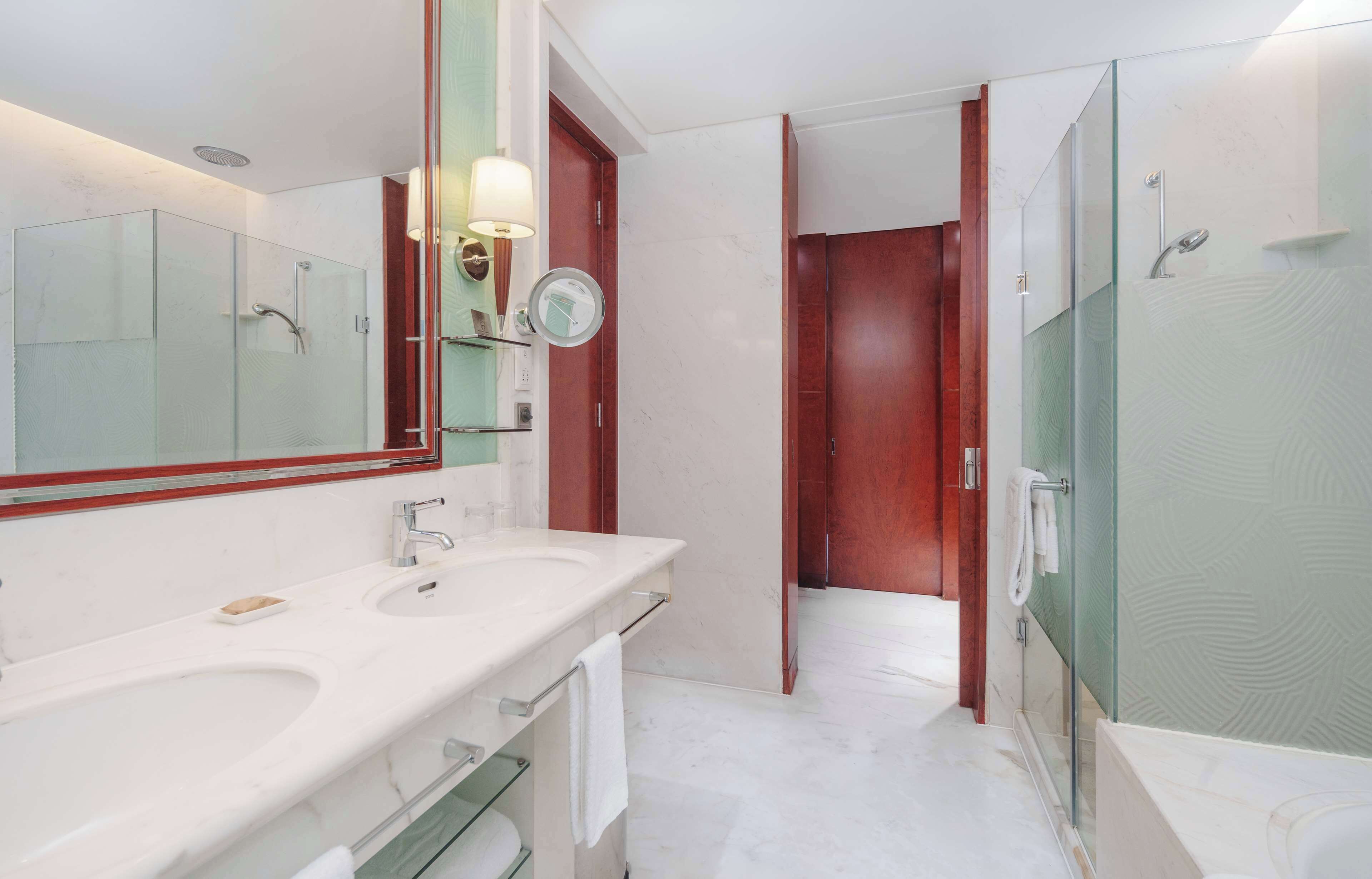 A modern bathroom with two sinks, a large mirror, and a glass-enclosed shower area.