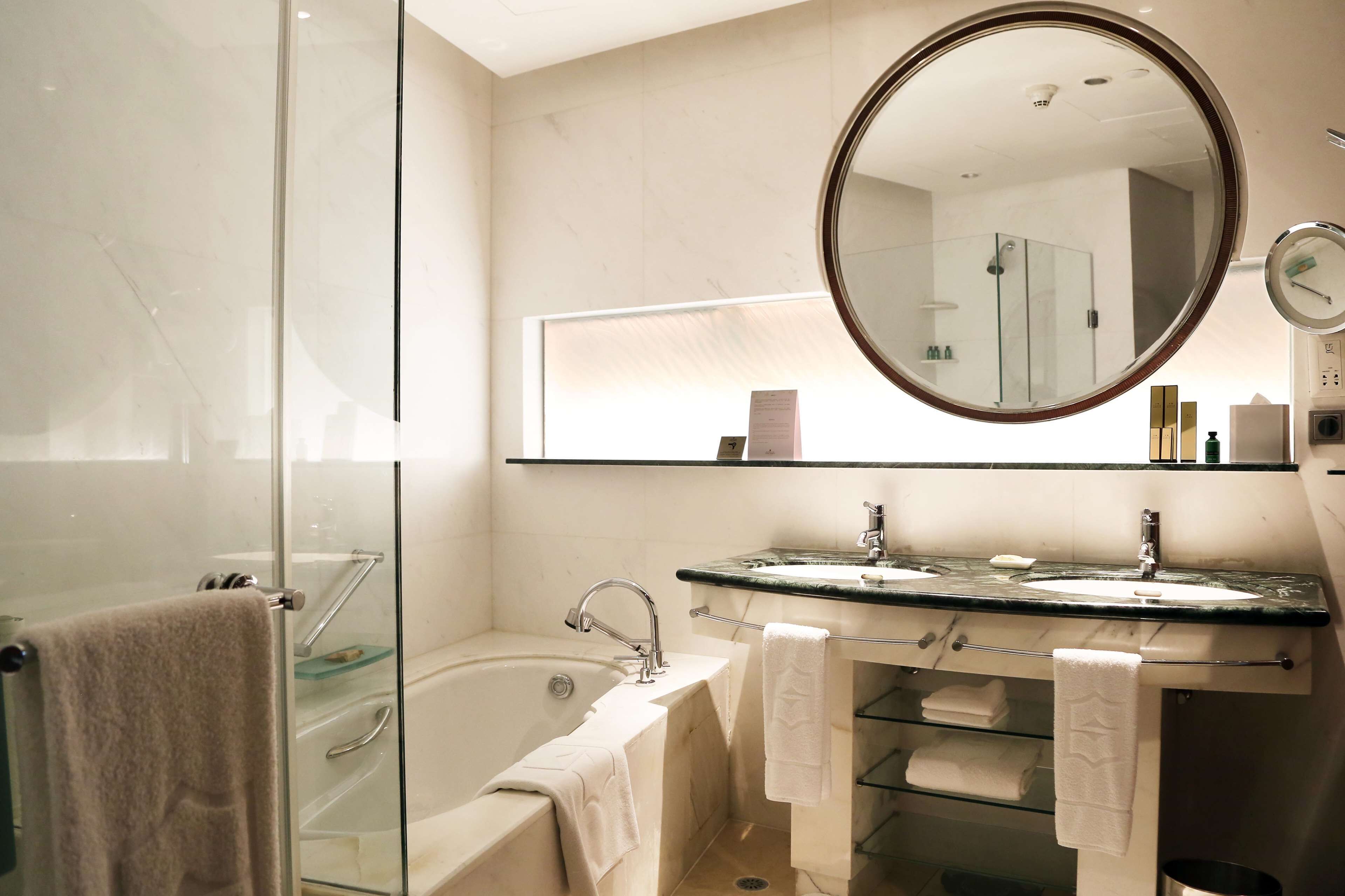 Ein modernes Badezimmer mit einer gläsernen Duschkabine, einer freistehenden Badewanne, einem großen Spiegel und einem Waschtisch mit Spüle und Handtuchhalter.