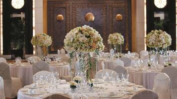 Un salón de banquetes con mesas redondas dispuestas para un evento formal, con centros de mesa florales y una elegante vajilla.