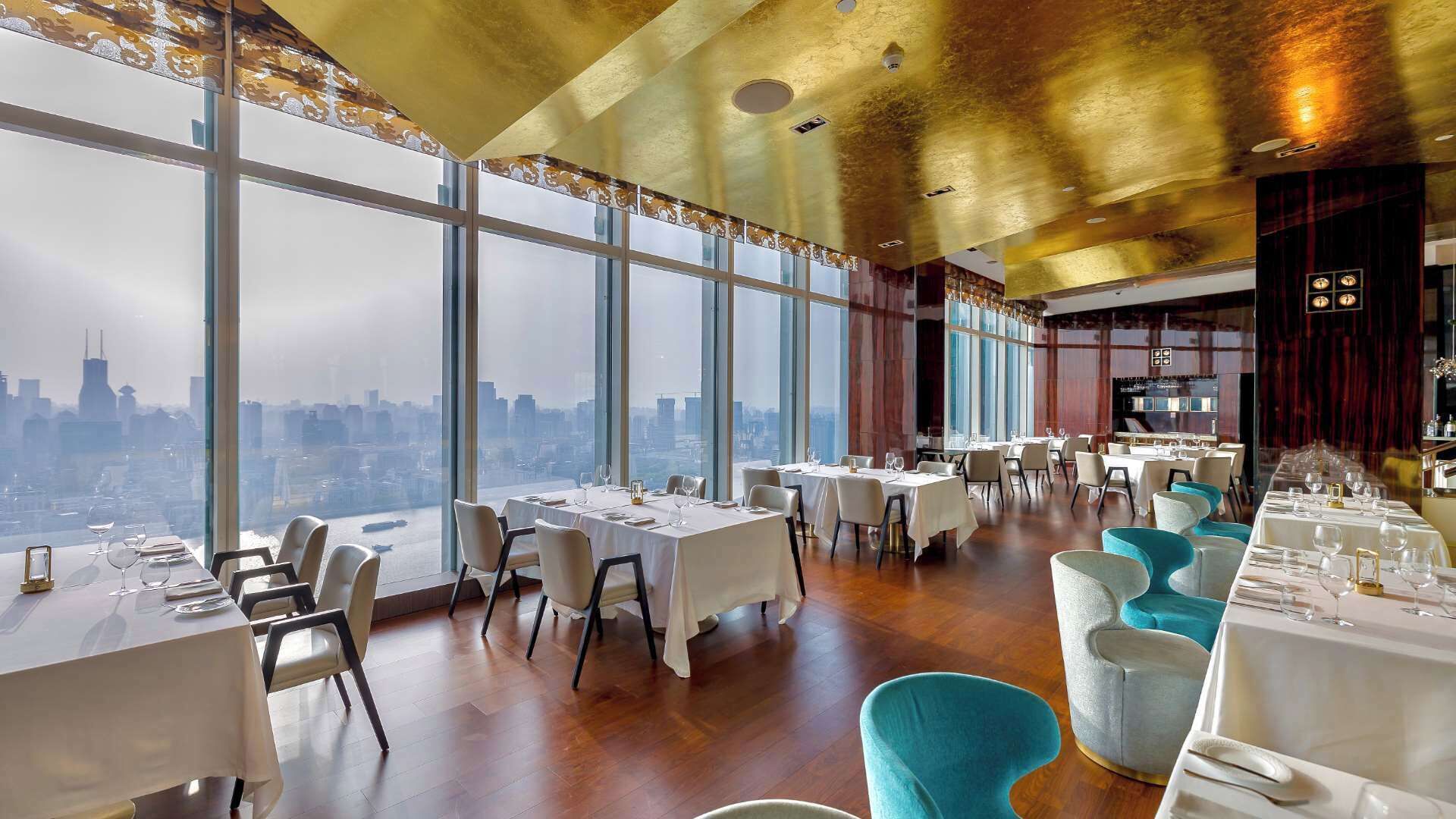 Un restaurante con mesas dispuestas para comer, amplias ventanas que ofrecen vista a la ciudad y un diseño de interiores moderno.