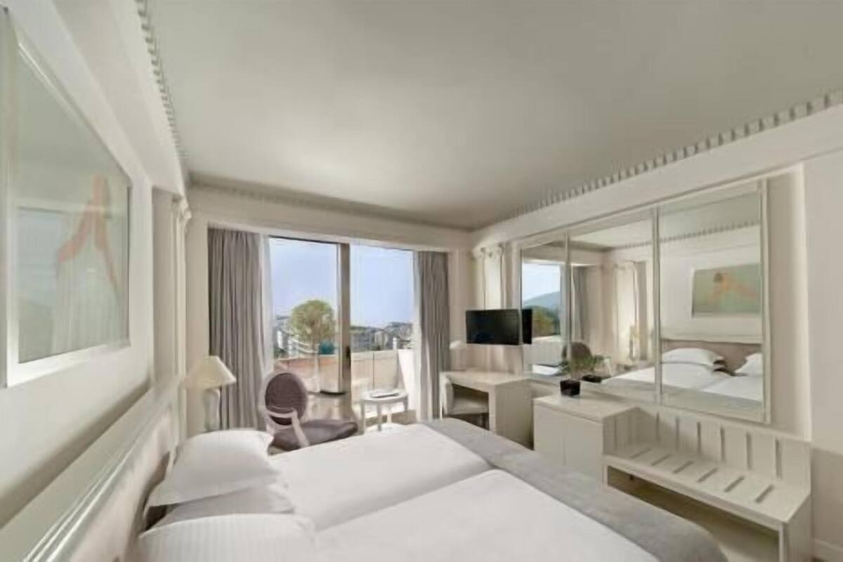 A hotel room with a large bed, a desk, a chair, a television, and a balcony with a view.