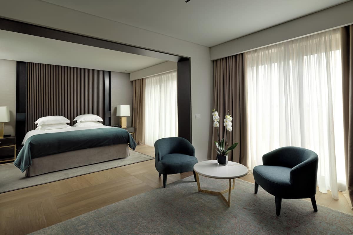 A modern hotel room with a large bed, two armchairs, a small round table, and a potted orchid.