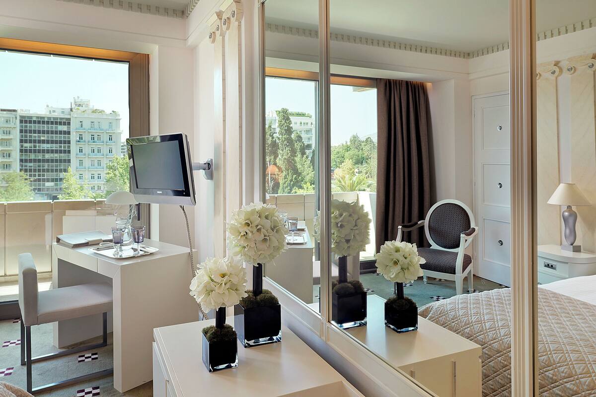 A hotel room with a desk, a chair, a bed, a TV, and a large mirror.
