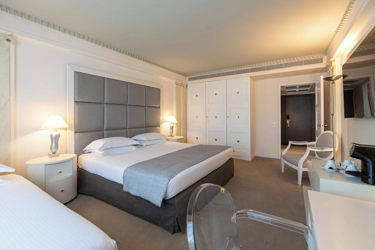 A hotel room with a large bed, a desk, a chair, and a wardrobe.